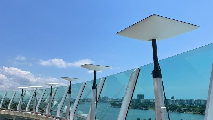 5 - Sewa Starlink Jakarta Rental Starlink Row of modern lamp posts along a glass railing on a waterfront boardwalk, city skyline in the distance under a blue sky.